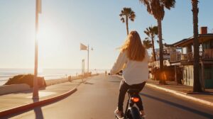 A woman rides an electric bike along a scenic coastal path at sunset, enjoying the ocean breeze and vibrant colors of the shoreline